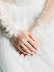 Hands of the bride with a wedding manicure and in a wedding ring close-up against the background of a wedding dress.