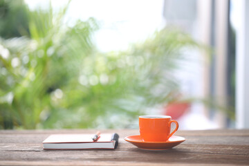 Orange coffee cup and notebook, and pen on wooden table outdoor
