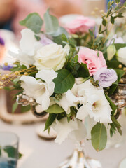 Floral decoration of the banquet table. A bouquet of white and lilac eustoma, pink roses, twigs, and leaves stands in a copper candlestick.