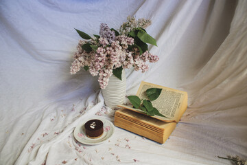 still life with lilac flowers fresh blooming on a valentine's day in a vase and book and dessert
