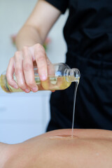 The masseur pours fragrant massage oil on the back of a woman in a spa salon. The therapist is preparing for a procedure for a relaxing treatment. Aromatherapy oil massage relax