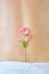 Fototapeta na wymiar Beautiful female body back and flowers. Aesthetics of a beautiful body
