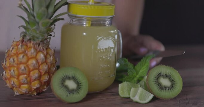 Natural juice mug with pineapple, kiwi and lime. With blurred woman's body in background.