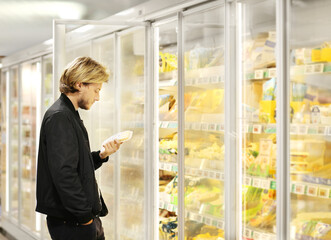  Man choosing frozen food from a supermarket freezer	, reading product information