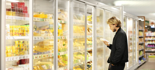  Man choosing frozen food from a supermarket freezer	, reading product information
