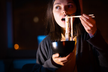 Girl eats noodles and watches video on a laptop.