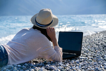 Girl in a hat works on a laptop on the beach,  seashore.