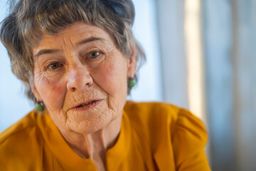 Old retired gray-haired woman in yellow blouse.