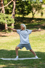 full length of cheerful senior man with grey hair smiling and working out with outstretched hands in park.