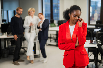 Young african woman crying because of the ridicule of colleagues. Racial discrimination in the office.