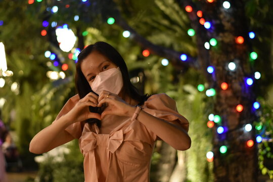 a woman going out at night raising hands to make a heart show love And there are flickering lights, a variety of bokeh colors, a blurry image.