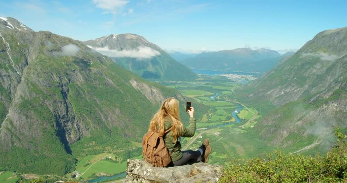 Adventure and traveling woman taking a photo of mountains on a phone while sitting and enjoying scenic views. A relaxed female tourist or vlogger recording a video of beautiful green nature