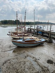 Landscape of boats in beautiful estuary water with sail boats moored in muddy beach by shore in Woodbridge Suffolk Eat Anglia with cloudy sky reflected in the river n Summer holiday no people