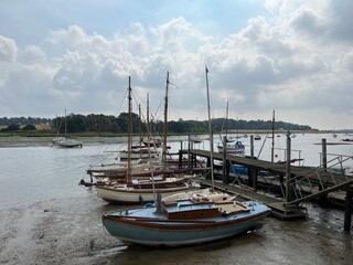 Landscape of boats in beautiful estuary water with sail boats moored in muddy beach by shore in Woodbridge Suffolk Eat Anglia with cloudy sky reflected in the river n Summer holiday no people