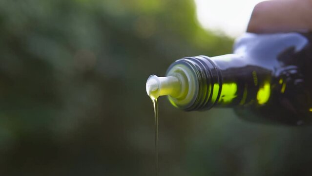 Close up of male hand pouring olive oil from glass bottle in slow motion.