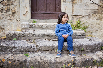 Little handsome baby boy sitting on ancient stone stairs outdoor in old city