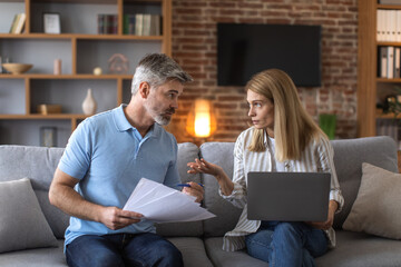 Serious mature caucasian husband and wife work with documents and laptop, pay taxes