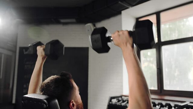 Bearded athlete athletic man bodybuilder training shoulders in the gym with dumbbells