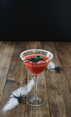 Terrifying red cocktail with spider on black background and wooden Halloween table with decoration. Vertical.