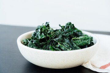 Teared curly green kale leaves in the plate with seasonings and olive oil on the kitchen table. Ingredients for kale chips or healthy salad meal. Healthy eating, dieting lifestyle. Selective focus.