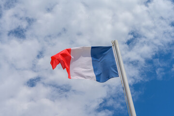 French flag waving in the wind. It is a beautiful sunny summer day, with blue sky and white clouds in the background.