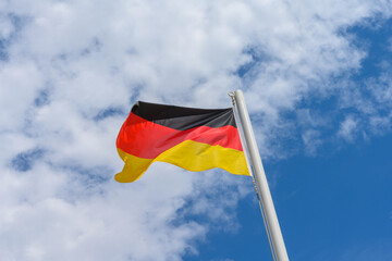 German flag waving in the wind. It is a beautiful sunny summer day, with blue sky and white clouds in the background.