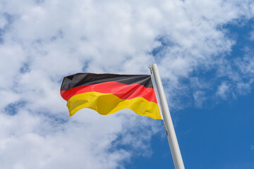 German flag waving in the wind. It is a beautiful sunny summer day, with blue sky and white clouds in the background.