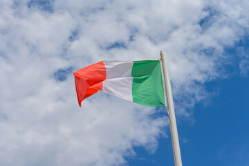 Italian flag waving in the wind. It is a beautiful sunny summer day, with blue sky and white clouds in the background.