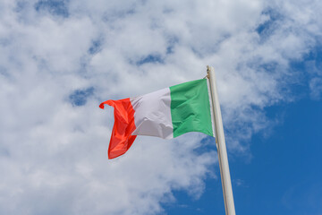Italian flag waving in the wind. It is a beautiful sunny summer day, with blue sky and white clouds in the background.