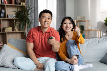 Happy asian man and woman watching TV at home