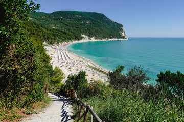 Naklejka premium Blue sea in sunny day close to the forest in the Conero natural park - Italy. During touristic season is full of umbrella and people.