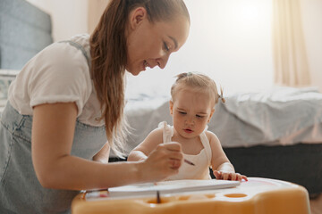 Little smiling girl painting with her mother at home while spending time together