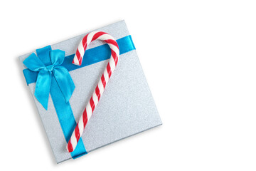 Christmas gift box with blue bow and a red and white candy in form cane on white background.