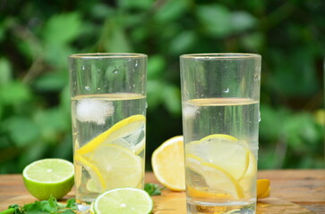 Fresh summer drink. Cold lemonade with mint lemon and lime on a nature outdoor background. Mojito summer refreshing cocktail with ice and mint