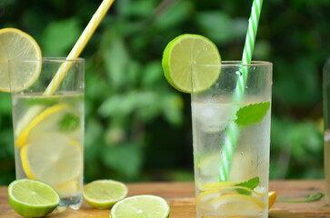 Fresh summer drink. Cold lemonade with mint lemon and lime on a nature outdoor background. Mojito summer refreshing cocktail with ice and mint