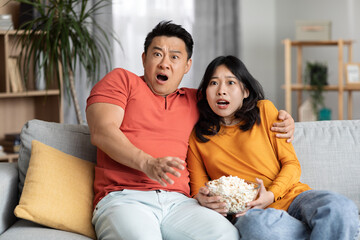 Thrilled korean man and woman watching spooky movie at home