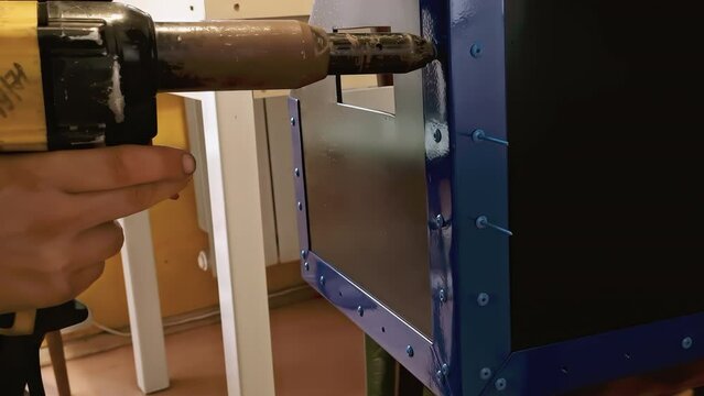 Male mechanic works with pneumatic tool rivet gun. Hands hold an electric riveting machine. Blind rivets for metal working. Slow motion.