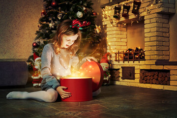 Happy kid girl with magic gift box at home near christmas tree and fireplace. Merry Christmas time...