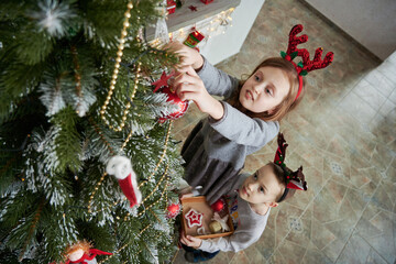 Children decorating Christmas tree at home. Boy and girl wear reindeer costume with ornament....