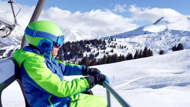Boy sit in sport outfit with helmet mask and ski going up
