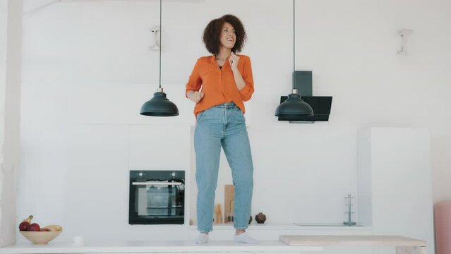Crazy funny dancing African American woman housewife with curly hair girl having fun in morning on kitchen standing on table dance before cooking cheerful energy movement at home celebrate weight loss