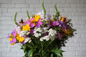 A bouquet of field various fresh flowers on a blurred brick wall background