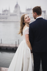Naklejka premium Beautiful gorgeous bride posing to groom and having fun, near Budapest parliament, space for text, wedding couple