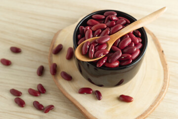 Fototapeta na wymiar red kidney beans in a black bowl and spoon on wooden background, front view, selective focus.