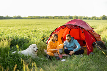Young couple have a picnic near the tent, while traveling with dog on nature. Man and woman...