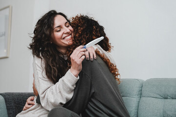 Latin gay female couple celebrating with pregnancy test at home - Focus on left mother face - Lgbt lesbian concept - obrazy, fototapety, plakaty
