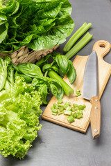 Chopped celery stalks, kitchen knife on cutting board. Lettuce leaves in wicker basket.