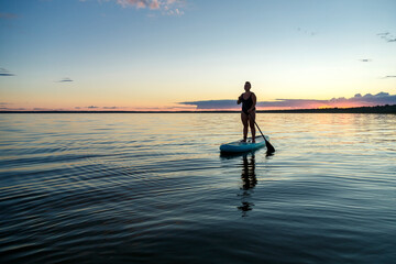 a woman in a closed swimsuit with a mohawk standing on a SUP board with an oar floats on the water...