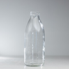 An empty glass bottle stands on a table on a gray background