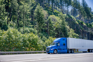 Bonnet big rig blue semi truck transporting cargo in dry van semi trailer driving on the highway...